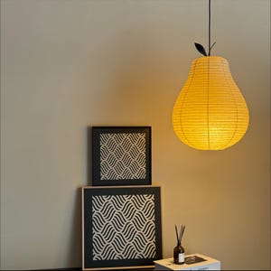 May include: A yellow pear-shaped pendant light hangs from the ceiling, casting a warm glow. Two framed prints with a black and white wave pattern are on a table. A small diffuser bottle and a stack of books complete the scene.