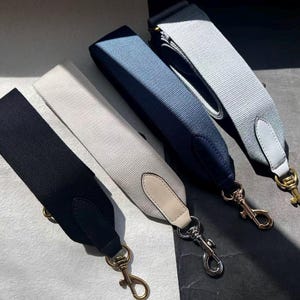 Può includere: Quattro tracolle colorate per borse in nero, bianco sporco, blu navy e grigio chiaro. Ogni cinturino ha una chiusura in metallo e dettagli in pelle. I cinturini sono realizzati in tessuto intrecciato e sono progettati per borse.