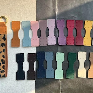 May include: A selection of leather keychain fobs in various colours, including brown, blue, pink, purple, red, yellow, and grey. A leopard print keychain strap with a gold ring is also included. These fobs are designed for crafting.