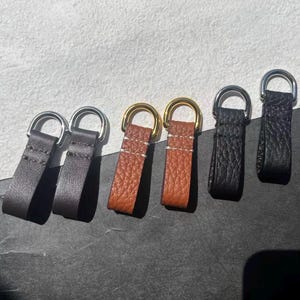 Peut inclure: Plusieurs tirettes de fermeture éclair en cuir de différentes couleurs, marron, noir et marron clair. Chaque tirette est dotée d'un anneau en D en métal pour l'attache. Le cuir est cousu pour la durabilité.