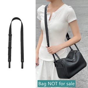 Op de afbeelding: Een zwarte leren crossbody tasriem met verstelbare lengte en goudkleurige hardware. De riem wordt getoond naast een zwarte leren handtas. De tekst "Bag NOT for sale" staat onderaan de afbeelding.