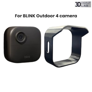 May include: Black Blink Outdoor 4 camera and a black protective cover. The camera is square with a lens and the word "blink" on the bottom. The cover is a curved shape with an opening for the camera.