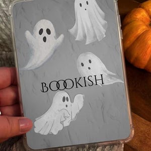 May include: A clear tablet case featuring a gray background with four white ghost illustrations and the text "BOOOKISH" printed in black. The ghosts are depicted in various positions, and the case has a smooth, transparent protective border.