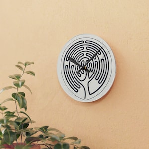 Puede incluir: Un reloj de pared circular con esfera blanca que presenta un patrón de laberinto de línea continua en azul oscuro. El reloj tiene manecillas negras para las horas y los minutos situadas en el centro. El diseño es limpio y sin números.