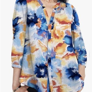 May include: A colourful blouse with a watercolour design in blue, orange, and white. It has a V-neck and three-quarter sleeves. The fabric looks light and airy, ideal for warmer weather. The blouse's pattern resembles an abstract floral design.
