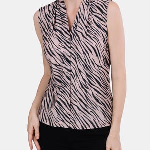 May include: Sleeveless top with a zebra stripe pattern in black and light pink. The top has a draped neckline and a button-down front. The model is wearing black pants.