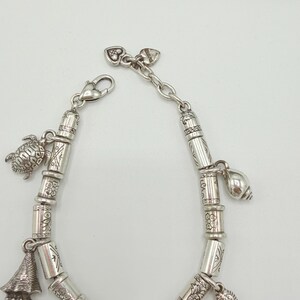 May include: A silver-toned charm bracelet featuring a series of cylindrical beads with engraved floral and geometric patterns. The bracelet includes dangling charms shaped like a sea turtle, a conch shell, and a seahorse, finished with a lobster clasp.