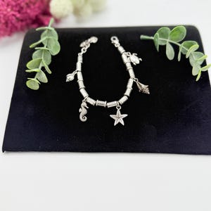 May include: A silver-toned charm bracelet featuring a series of cylindrical metal beads interspersed with various sea-themed charms, including a seahorse, a starfish, a sea shell, and a sea turtle, secured with a metal lobster claw clasp.