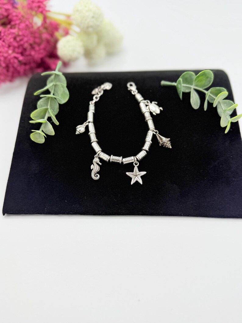 May include: A silver-toned charm bracelet featuring a series of cylindrical metal beads interspersed with various sea-themed charms, including a seahorse, a starfish, a sea shell, and a sea turtle, secured with a metal lobster claw clasp.