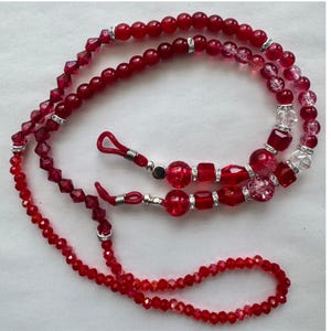 May include: A red beaded eyeglass chain featuring a mix of smooth round beads, faceted crystal-like beads, and crackled glass beads. The chain includes small silver-toned spacers with embedded clear stones and red silicone loops at the ends.