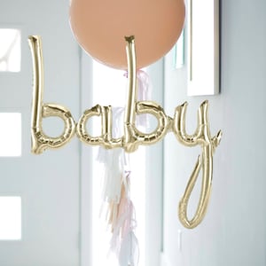 Puede incluir: Globos de letras de lámina dorada que deletrean "baby" con un globo de color melocotón y una guirnalda de borlas blancas y melocotón.