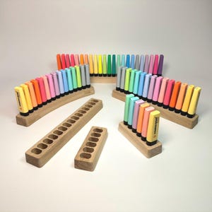 May include: A collection of colorful highlighters arranged in wooden holders. The highlighters are in various shades, including yellow, orange, pink, green, and blue. The wooden holders are rectangular and curved, with individual slots for each highlighter. The image showcases stationery organization.