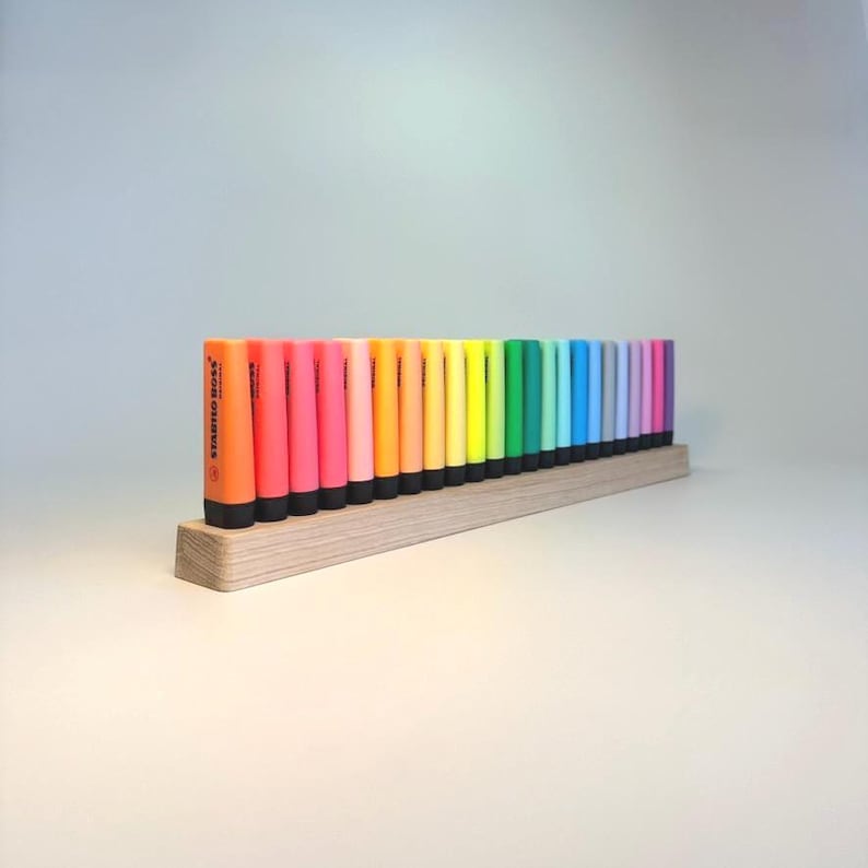 May include: A collection of colorful highlighters in a wooden holder. The highlighters are arranged in a rainbow spectrum, with colors ranging from orange to purple. The brand name "STABILO BOSS" is visible on the orange highlighter.
