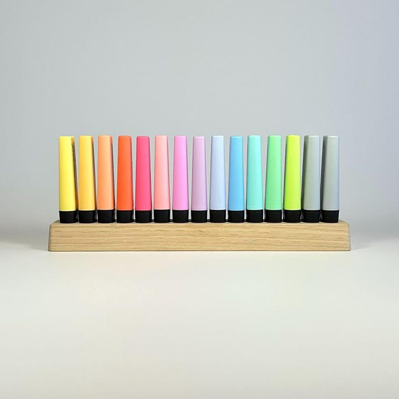 May include: A set of twelve colorful, cone-shaped objects in a wooden holder. The objects are arranged in a row, with colors ranging from yellow to gray. Each object has a black base. The wooden holder is rectangular and has a natural wood finish.