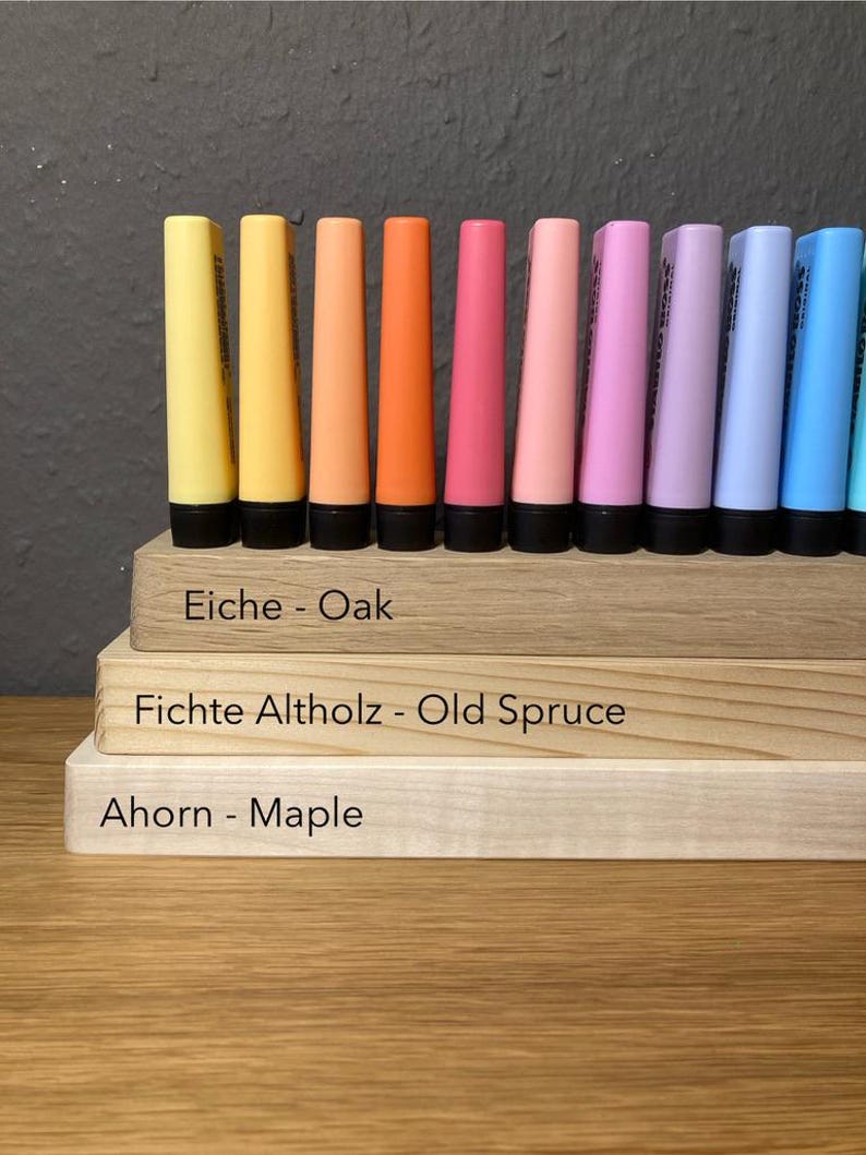 May include: A collection of colorful, conical-shaped markers in shades of yellow, orange, pink, purple, and blue, arranged on wooden blocks. The blocks are labeled with wood types: Oak, Old Spruce, and Maple.