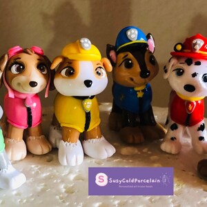 Könnte beinhalten: Eine Sammlung von sieben bunten Paw Patrol-Figuren. Jede Figur ist ein anderer Charakter, der eine Uniform in verschiedenen Farben trägt, darunter Grün, Rosa, Gelb, Blau, Rot und Orange. Die Figuren stehen auf einer weißen Oberfläche.