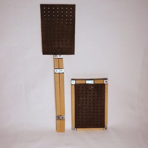Puede incluir: Dos matamoscas de madera. Uno es rectangular con un mango largo, el otro es un rectángulo más pequeño. Ambos tienen una superficie perforada marrón oscuro y mangos de madera marrón claro con bisagras metálicas.