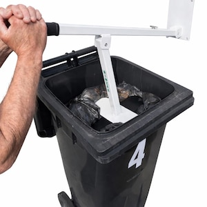 May include: A white metal trash compactor tool with a black handle grip and the word BINNEE printed in green on the vertical arm. The device is positioned inside a black plastic wheeled trash bin marked with the white number 4 on the front side.