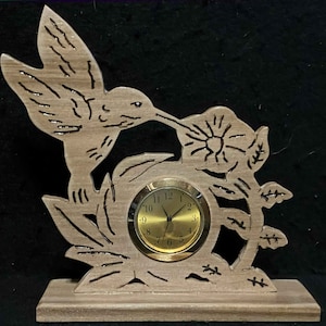 May include: A wooden clock with a hummingbird design. The hummingbird is perched on a branch with a flower. The clock face is gold with black numbers and hands.