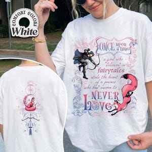 May include: White t-shirt with a fantasy-themed design. The front features a graphic of an archer, text that reads "Once upon a time", and a fox. The back has a fox and bow and arrow design.