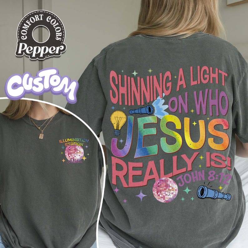 May include: Dark gray t-shirts with the text "Shining a Light on Who Jesus Really Is!" in colorful letters. The design includes a lightbulb, a telescope, and a disco ball. The shirt also has the text "John 8:12".