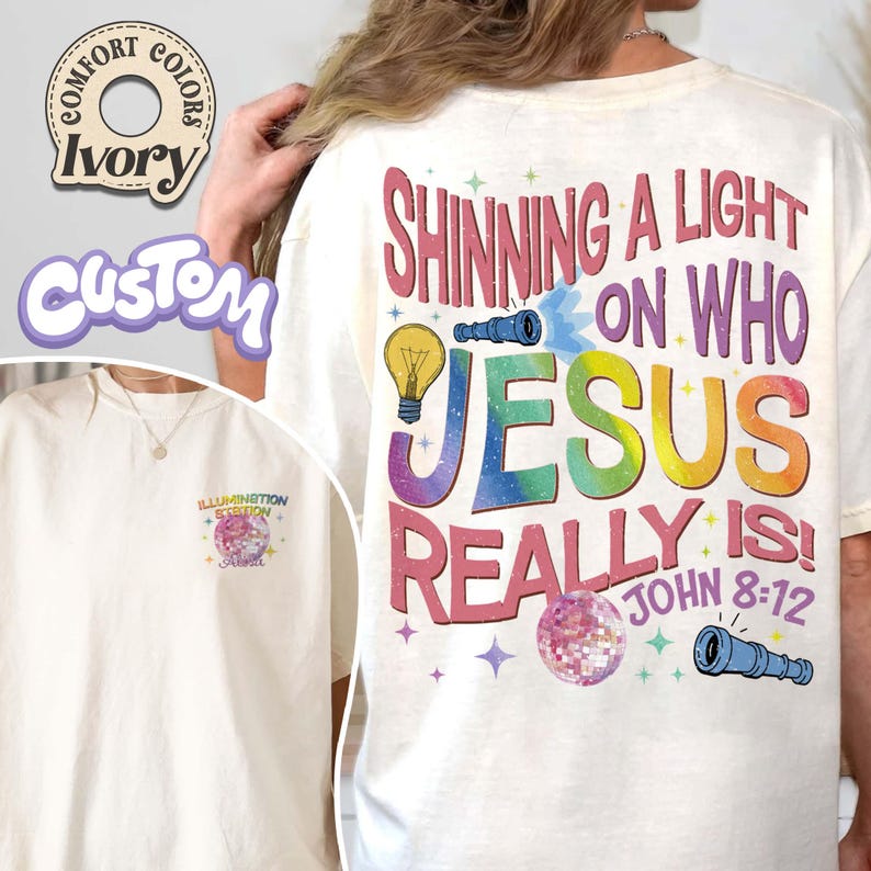 May include: Ivory-colored t-shirt with the text "Shining a Light on Who Jesus Really Is!" in a colorful, rainbow design. The shirt also features a small graphic on the front. The shirt is a Comfort Colors brand.
