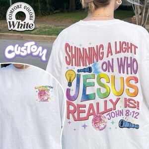 May include: White t-shirt with the text "Shining a Light on Who Jesus Really Is!" in colorful letters. The shirt also features a lightbulb, telescope, and disco ball graphic. The left side of the shirt has the text "Illumination Station" and the name "Alisa".
