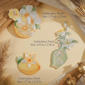 May include: Three embroidered patches featuring botanical and fruit designs. One patch shows white flowers with a citrus slice, measuring 2.76 in x 2.76 in. Another is a tall vase with lilies, 4.33 in x 2.36 in. The third is a lemon, 1.77 in x 1.57 in.