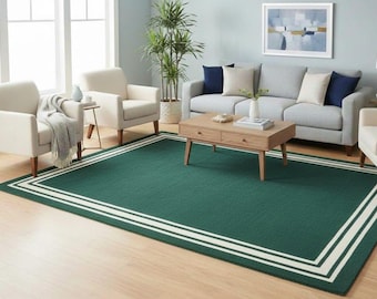 May include: A living room scene featuring a large, rectangular green rug with a white border. The room includes two cream-colored armchairs, a gray sofa, a wooden coffee table, and a potted plant. A painting hangs on the wall.
