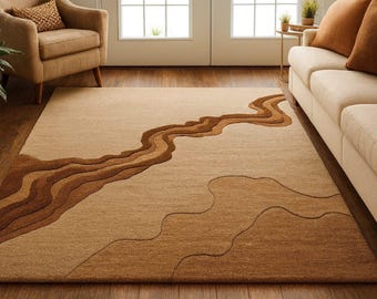 May include: Beige area rug with a flowing, layered design in shades of brown. The rug's pattern resembles a river or landscape, adding a natural element to the room. The rug is rectangular and placed on a hardwood floor.