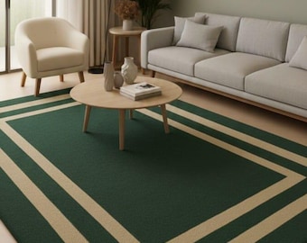 May include: A rectangular green rug with a beige border in a living room setting. The rug is centered in front of a gray sofa and a round wooden coffee table. The room has a neutral color palette with artwork on the wall.