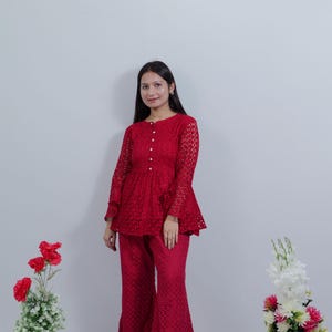 Può includere: Un top in pizzo rosso e pantaloni abbinati. Il top ha maniche lunghe, vita a peplo e dettagli con bottoni. I pantaloni sono svasati. L'outfit è di un colore rosso vibrante. Adatto per un'occasione speciale.