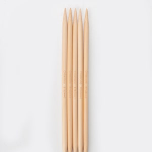 May include: Five wooden knitting needles with pointed tips. The needles are labeled "ChiaoGoo 8 (5.0mm)".