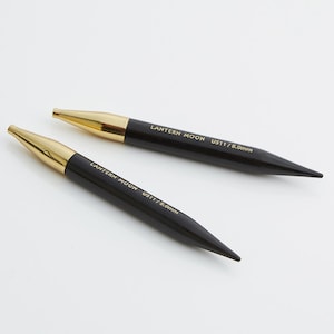 May include: Two black knitting needles with gold tips. The needles are labeled "LANTERN MOON US11/8.0mm".