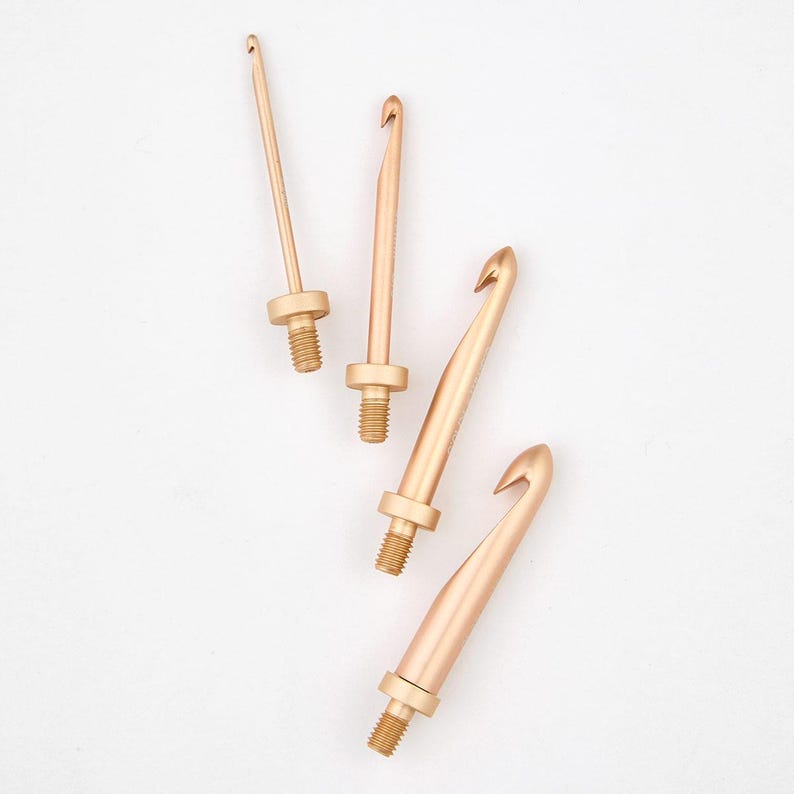 May include: Four gold-coloured crochet hooks of different sizes. The hooks are made of metal and have a smooth finish.