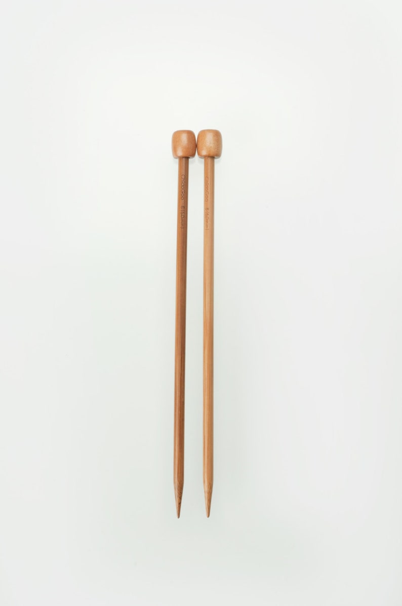 May include: Two wooden knitting needles with rounded tops and pointed ends. One needle is a medium brown color, and the other is a lighter tan color. The text "ChiaoGoo 8.00mm" is printed on the side of each needle.