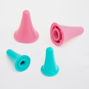 May include: Four plastic knitting needle point protectors in pink and teal. The protectors are cone-shaped with a wide base and a rounded tip. Two are pink, and two are teal, all on a white background.