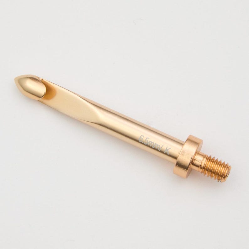 May include: A gold-coloured 6.5 mm crochet hook with a threaded end. The hook is made of metal and has a smooth, polished finish.