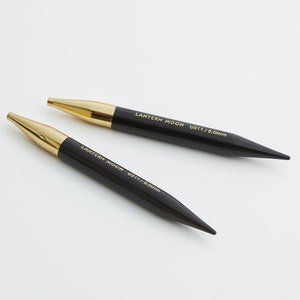 May include: Two black double-pointed knitting needles with gold tips. The needles are labeled "LANTERN MOON US11/8.0mm".