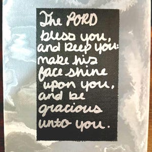 Puede incluir: Una obra de arte en lienzo con un centro rectangular negro con una inscripción blanca que dice: "El SEÑOR te bendiga y te guarde: haga resplandecer su rostro sobre ti y tenga de ti misericordia". El fondo tiene un efecto marmolado.