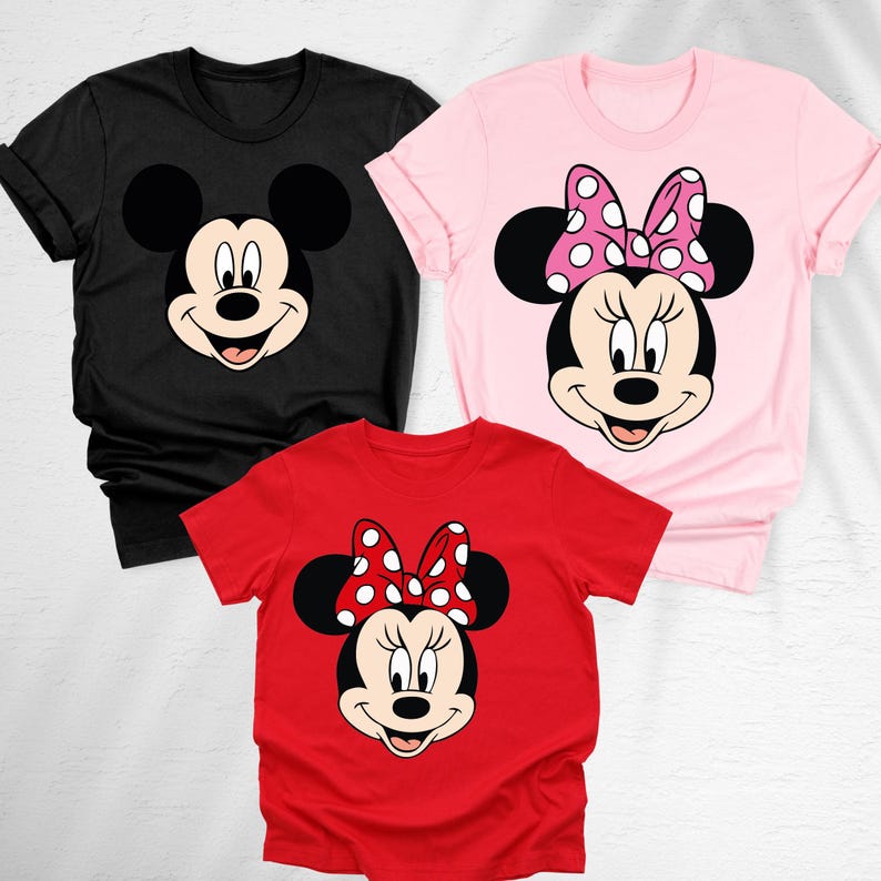 May include: Three t-shirts featuring cartoon character faces. A black t-shirt with Mickey Mouse's face, a pink t-shirt with Minnie Mouse's face and a red t-shirt with Minnie Mouse's face. Minnie Mouse has a polka dot bow.