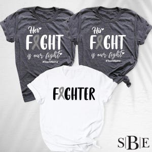 May include: Three t-shirts with text and a gray ribbon design. Two dark gray shirts read "Her Fight is our fight" and "His Fight is our fight". A white shirt says "Fighter". All shirts have a crew neck.