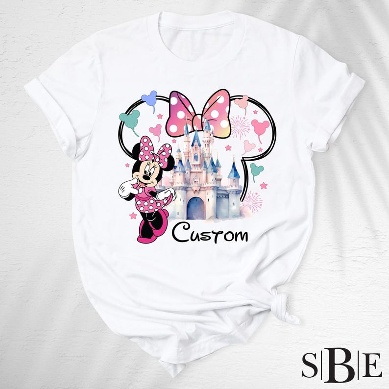 May include: White t-shirt featuring a Minnie Mouse graphic with a pink polka dot bow, a castle, and the word "Custom". The design includes a Minnie Mouse silhouette, hearts, and stars.
