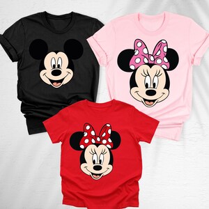May include: Three t-shirts featuring cartoon character faces. A black t-shirt with Mickey Mouse's face, a pink t-shirt with Minnie Mouse's face and a red t-shirt with Minnie Mouse's face. Minnie Mouse has a polka dot bow.