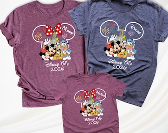 May include: Three short-sleeved t-shirts in maroon and heather blue featuring a white Mickey Mouse ear outline graphic. The design includes Disney characters, a castle, fireworks, and the text "Disney Trip 2026" with "Mommy", "Daddy", and "Melissa".