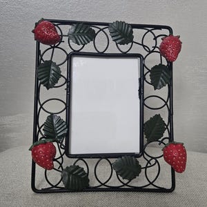May include: Black metal picture frame with a rectangular aperture. The frame is decorated with red strawberries and green leaves. The frame has a decorative, openwork design.