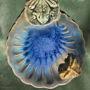 Peut inclure: Un plat en céramique avec un motif de grenouille et de fleur. Le plat en forme de feuille est émaillé bleu et vert. Une grenouille verte est au sommet. Une fleur brune est sur le côté.