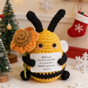 May include: A handmade crochet bee with black antennae, wings, and legs, holding a flower. The bee is yellow with black stripes and has a small sign that reads "BEE kind whenever possible, but sting like a WASP when you need to."
