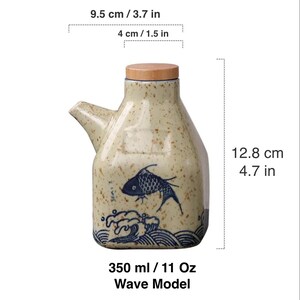 May include: Ceramic oil dispenser, 4.7 inches tall, with a wooden lid and spout. The beige bottle features a blue fish and wave design. It holds 11 oz and is 3.7 inches wide.