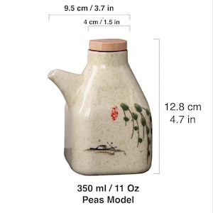 May include: A ceramic oil dispenser with a light beige speckled finish. It features a wooden lid and a spout. The design includes a painted floral and landscape motif. The dispenser is 4.7 inches tall and holds 11 oz.